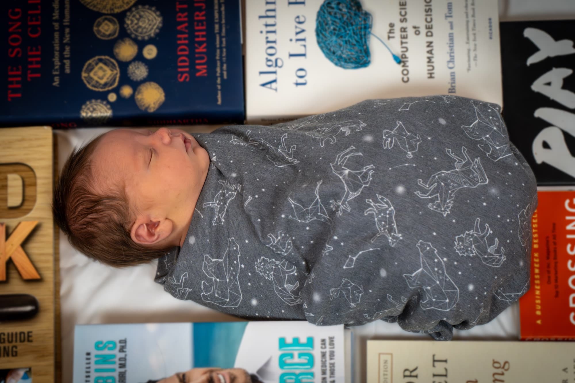 Newborn swaddled in a constellation wrap, surrounded by books